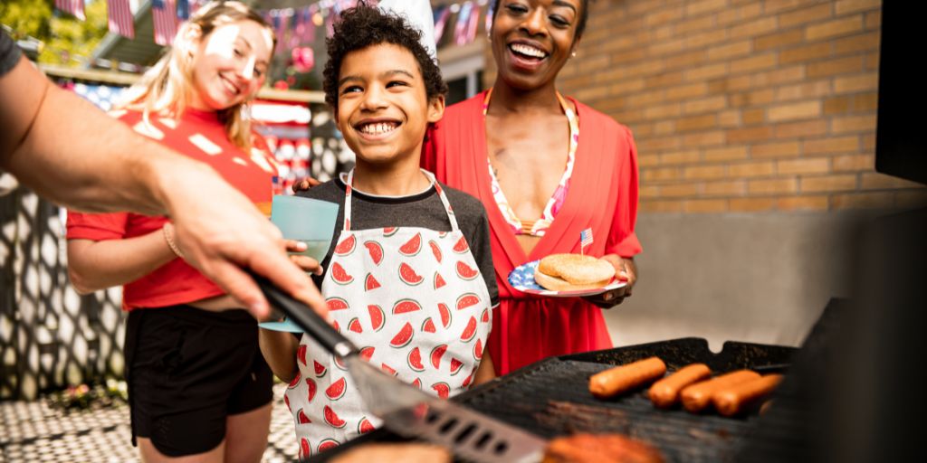 Family gathered around a grill with hot dogs 