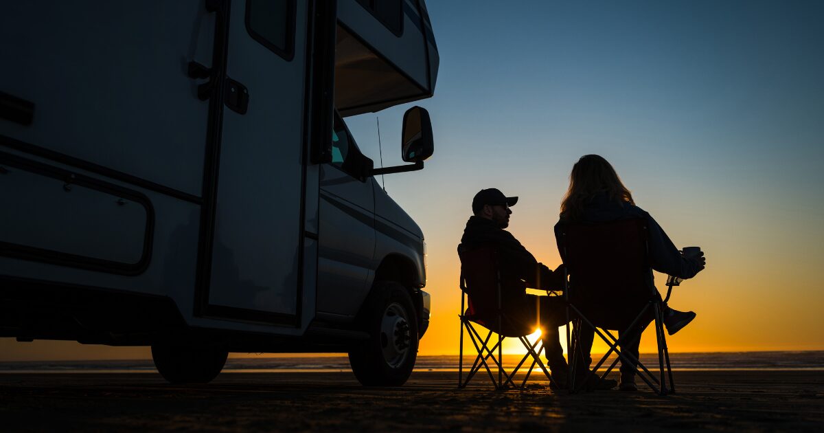 Two people sitting in front of an RV at sunset